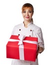 Portrait of young beautiful red-haired woman doctor or nurse in white special uniform standing holding big present box with ribbon