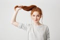 Portrait of young beautiful redhead girl touching her hair tail looking at camera over white background. Royalty Free Stock Photo