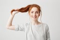 Portrait of young beautiful redhead girl touching her hair tail looking at camera over white background. Royalty Free Stock Photo