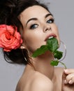 Portrait of young beautiful sexy brunette naked woman in circle earrings with rose in hair biting rose leaf