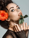 Portrait of young beautiful sexy brunette naked woman in circle earrings with rose in hair biting rose leaf
