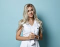 Portrait of young beautiful sexy smiling woman with long blonde wavy hair in white dress standing over blue wall Royalty Free Stock Photo