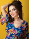 Portrait of young beautiful smiling brunette in blue low-necked dress with bright floral print holding hand up in her hair