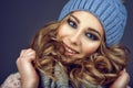 Portrait of young beautiful smiling girl with professional make up and curly hair coming out of her blue knitted hat