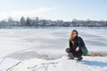 Portrait of a young beautiful smiling red hair european girl sitting near the frozen river Royalty Free Stock Photo