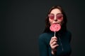 Portrait of a young beautiful stylish girl wearing red drop shaped sunglasses holding a red lollipop and biting it in a Royalty Free Stock Photo