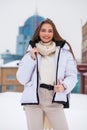 Fshion girl in a white down jacket and beige pants posing outdoors in winter