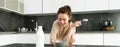 Portrait of young beautiful woman in bathrobe, eating cereals for breakfast, leans on kitchen worktop, looking at her Royalty Free Stock Photo