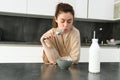 Portrait of young beautiful woman in bathrobe, eating cereals for breakfast, leans on kitchen worktop, looking at her Royalty Free Stock Photo