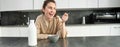 Portrait of young beautiful woman in bathrobe, eating cereals for breakfast, leans on kitchen worktop, looking at her Royalty Free Stock Photo