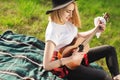 Portrait of a young beautiful woman in a black hat. Girl sitting on the grass and playing guitar Royalty Free Stock Photo