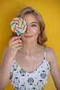Portrait of young beautiful woman with curly long hair and playful hairstyle. Smiling. Holding and licking a lollipop.