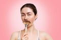 Portrait of a young beautiful woman, gravely holding a fluffy brush in the form of a mustache. Pink background. The concept of
