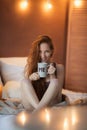 Portrait of young beautiful woman her hands holding cup of coffee morning cold winter time in her white bedroom. Happy Royalty Free Stock Photo