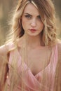 Portrait of young beautiful woman with make up outdoors. blond girl with long hair and in a pink dress in field in grass. close up Royalty Free Stock Photo