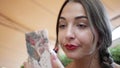 Portrait of a young beautiful woman, she paints her lips with red lipstick and looks in a small mirror. outdoors