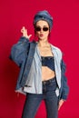 Portrait of young beautiful woman posing in stylish jeans clothes and trendy sunglasses against red studio background Royalty Free Stock Photo