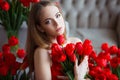 Portrait of young beautiful woman in red dress with tulips in luxury interior.