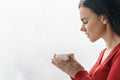 Portrait of young beautiful woman in red sweater drinking coffee. Female standing near window in skyscraper in morning on cloudy Royalty Free Stock Photo