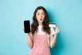 Portrait of young beautiful woman showing plastic credit card and empty smartphone screen, look amused and interested