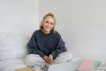 Portrait of young beautiful woman sitting on bed with laptop and notebooks, working from home, freelancing. Female Royalty Free Stock Photo