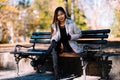 Portrait of young beautiful woman sitting on the bench in stylish warm outfit in sunny autumn day in park. Casual lifestyle in the Royalty Free Stock Photo