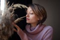 Portrait of a young beautiful woman touching wheat spikelets. Blonde girl wearing pink sweater in scandinavian interior Royalty Free Stock Photo