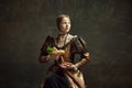 Portrait of young beautiful woman in vintage, elegant dress holding giant hot dog against dark green background. Fast Royalty Free Stock Photo