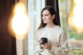 Portrait of a young beautiful woman in a warm sweater and with a cup of hot drink at home on the background of a window Royalty Free Stock Photo