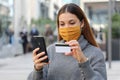 Portrait of young beautiful woman wearing protective mask chill out and make payment through credit card and smartphone app in the
