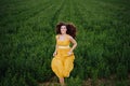 Portrait of young beautiful woman wearing a yellow dress running in a green field. Summertime and lifestyle Royalty Free Stock Photo