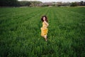 Portrait of young beautiful woman wearing a yellow dress running in a green field. Summertime and lifestyle Royalty Free Stock Photo