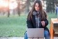 Portrait of young beautiful woman working remotely in a park. She sitting on a bench she is focused as she types on her laptop Royalty Free Stock Photo