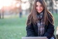 Portrait of young beautiful working woman sitting on a bench in a park. She smiles looking into the camera as she types on her Royalty Free Stock Photo