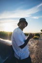 Portrait of a young black handsome man wearing a bucket hat posing outside by his car at sunset Royalty Free Stock Photo