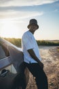 Portrait of a young black handsome man wearing a bucket hat posing outside by his car at sunset Royalty Free Stock Photo