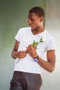 Portrait of Young Black Man holding white rose flowr, standing against wall, thinking