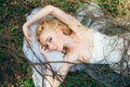 Portrait of young blond bride with veil that lies on earth under the branches and hands up