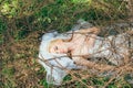 Portrait of young blond bride with veil that lies on earth under the branches