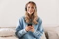 Portrait of young blond girl 20s wearing headphones using smartphone and listening to music at home Royalty Free Stock Photo