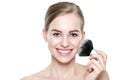 Portrait of a young blond woman applying dry cosmetic tonal foundation on her face using make up brush. Beauty portrait.