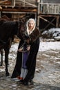 Portrait of a young blond woman in a black cloak with a horse. Royalty Free Stock Photo