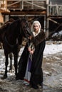 Portrait of a young blond woman in a black cloak with a horse. Royalty Free Stock Photo