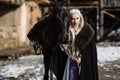 Portrait of a young blond woman in a black cloak with a horse. Royalty Free Stock Photo