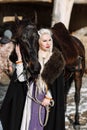 Portrait of a young blond woman in a black cloak with a horse. Royalty Free Stock Photo