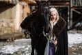 Portrait of a young blond woman in a black cloak with a horse. Royalty Free Stock Photo