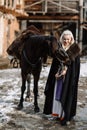 Portrait of a young blond woman in a black cloak with a horse. Royalty Free Stock Photo