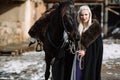 Portrait of a young blond woman in a black cloak with a horse. Royalty Free Stock Photo