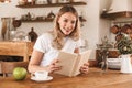 Portrait of young blond woman reading book and drinking coffee while sitting in cozy cafe indoor Royalty Free Stock Photo