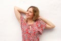 Young blond woman smiling with hands behind head against white background